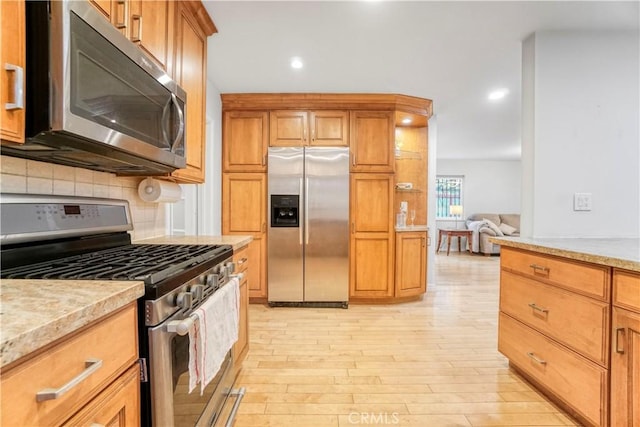 kitchen featuring decorative backsplash, brown cabinetry, light wood-type flooring, and appliances with stainless steel finishes