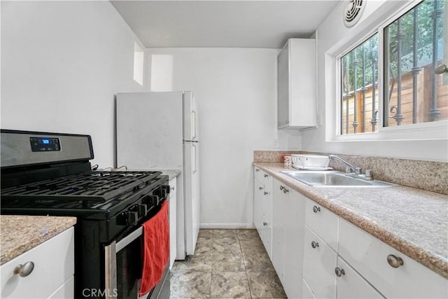 kitchen featuring gas range oven, white cabinetry, light countertops, and a sink