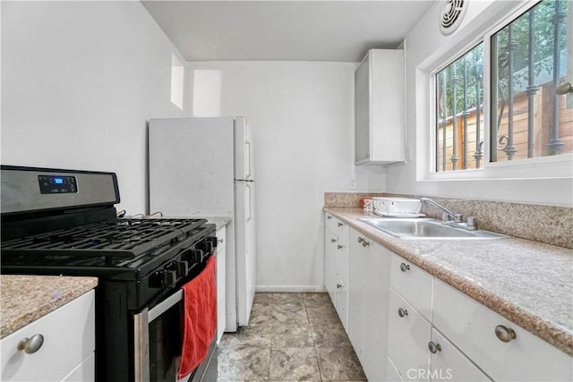 kitchen featuring light countertops, baseboards, white cabinetry, stainless steel gas range oven, and a sink