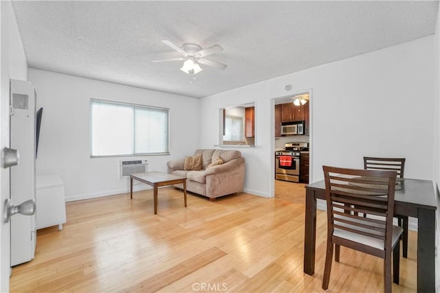 living room with a wall mounted air conditioner, a textured ceiling, ceiling fan, and light wood-style flooring