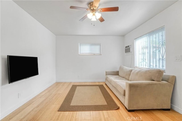 living area featuring a ceiling fan, a wall unit AC, baseboards, and light wood finished floors