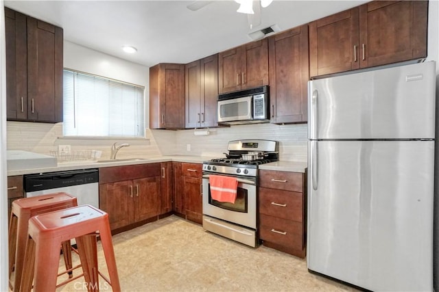 kitchen featuring light floors, light countertops, decorative backsplash, appliances with stainless steel finishes, and a sink