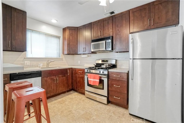 kitchen featuring light countertops, decorative backsplash, a sink, appliances with stainless steel finishes, and light floors