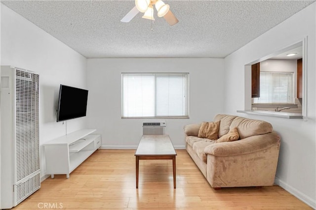 living room with a wall mounted AC, a textured ceiling, light wood-style flooring, a heating unit, and ceiling fan