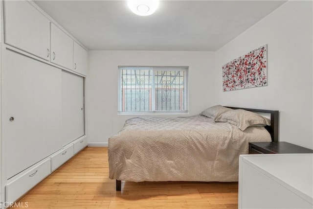 bedroom with light wood finished floors, a baseboard radiator, and a closet