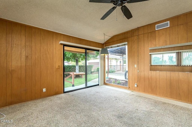 carpeted empty room featuring a textured ceiling, vaulted ceiling, wooden walls, and ceiling fan