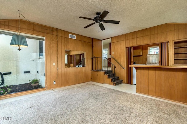 interior space featuring a textured ceiling, wood walls, light colored carpet, and lofted ceiling