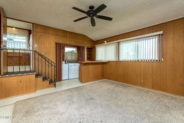 unfurnished room featuring vaulted ceiling, washing machine and clothes dryer, wood walls, a textured ceiling, and ceiling fan