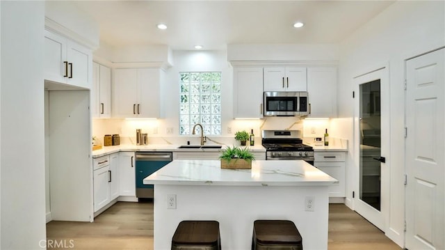 kitchen with a breakfast bar area, appliances with stainless steel finishes, a center island, white cabinetry, and a sink