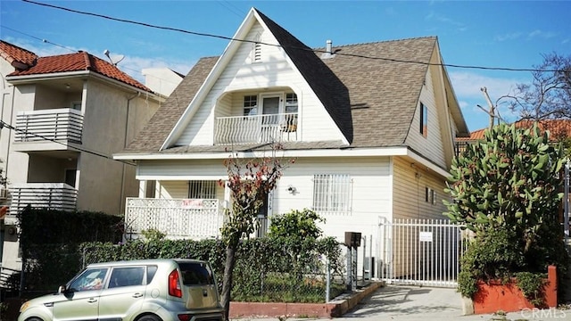 view of front facade with roof with shingles, a fenced front yard, and a balcony