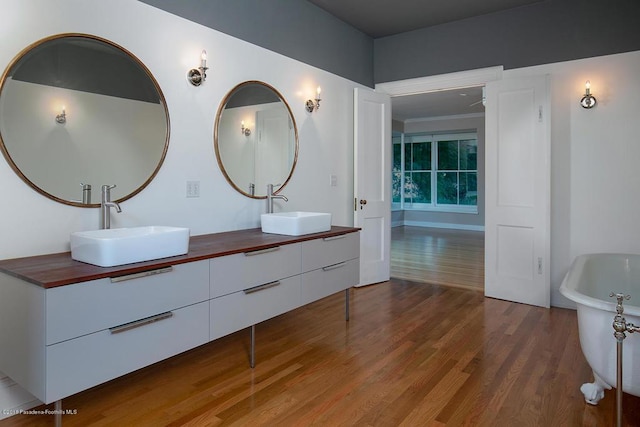 bathroom featuring a freestanding bath, double vanity, wood finished floors, and a sink