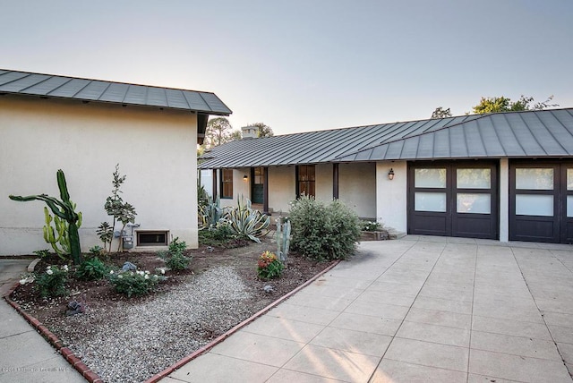 view of front of property with metal roof, an attached garage, driveway, stucco siding, and a standing seam roof