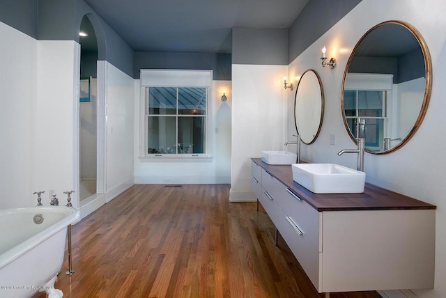 bathroom featuring double vanity, wood finished floors, a soaking tub, and a sink