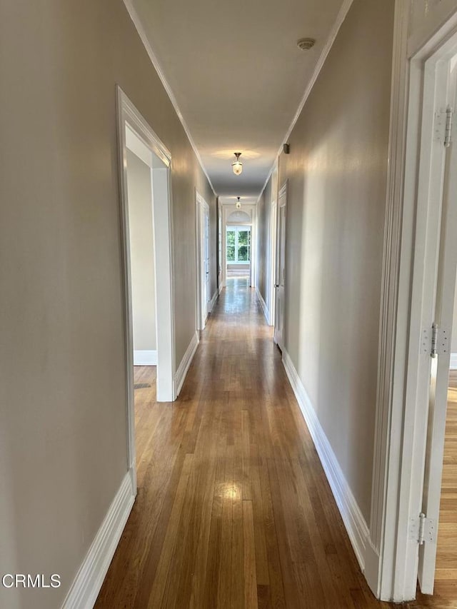 corridor with ornamental molding, wood finished floors, and baseboards