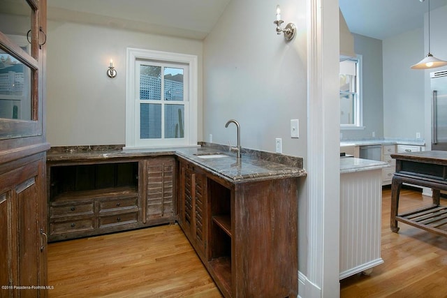 kitchen featuring light wood-style flooring, glass insert cabinets, pendant lighting, and a sink