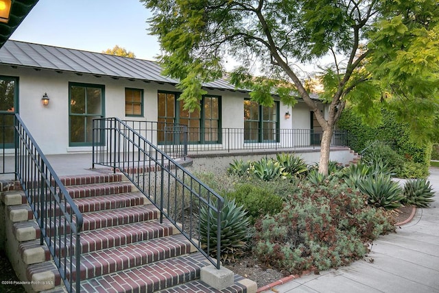 view of front of property featuring a standing seam roof, stairway, metal roof, and stucco siding