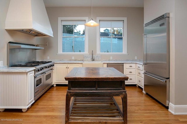 kitchen featuring premium appliances, premium range hood, a sink, white cabinetry, and hanging light fixtures