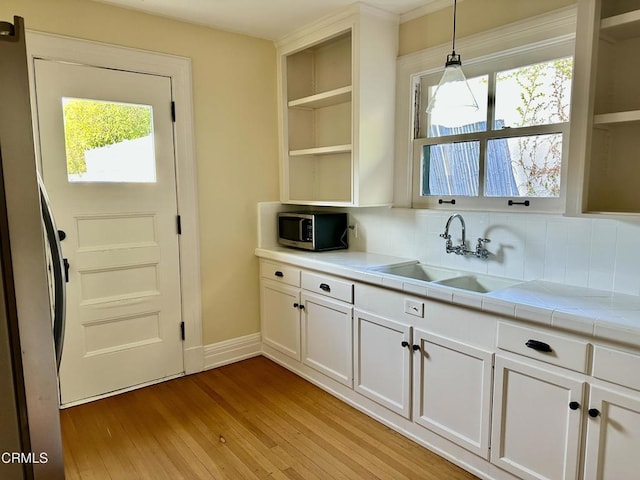 kitchen featuring tile countertops, open shelves, stainless steel appliances, white cabinetry, and a sink