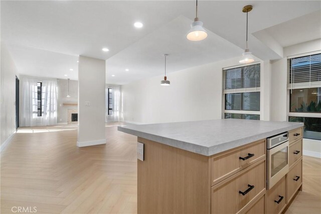 kitchen with hanging light fixtures, a kitchen island, stainless steel microwave, light brown cabinets, and light parquet floors