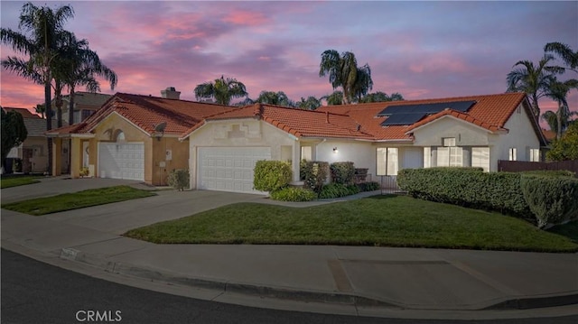 mediterranean / spanish-style home with concrete driveway, a tiled roof, an attached garage, roof mounted solar panels, and stucco siding