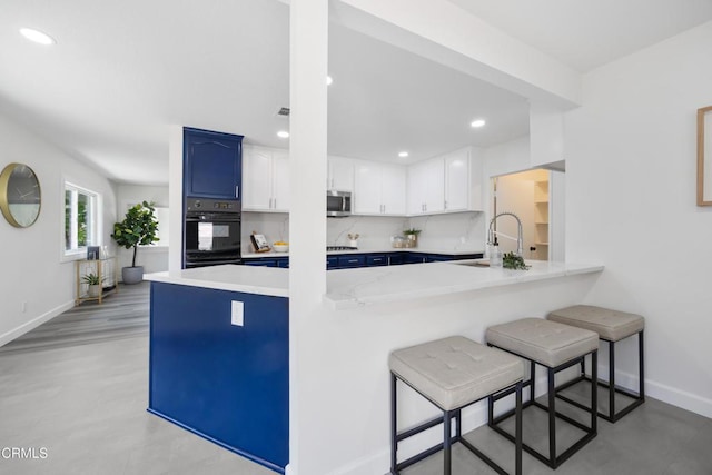 kitchen with kitchen peninsula, black oven, sink, white cabinets, and a breakfast bar area