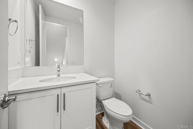 bathroom with toilet, wood finished floors, vanity, and baseboards
