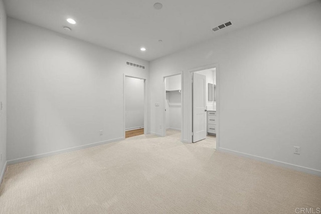 unfurnished bedroom with a walk in closet, light colored carpet, baseboards, and visible vents