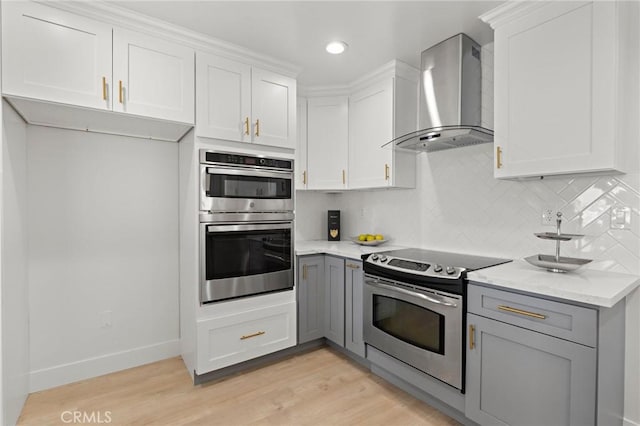 kitchen with wall chimney range hood, stainless steel appliances, white cabinets, and light stone counters