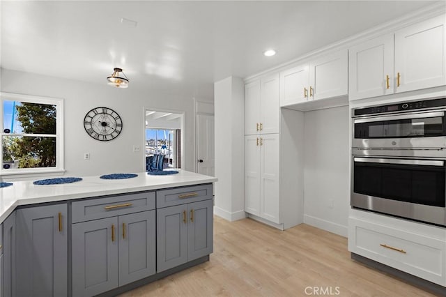 kitchen with stainless steel double oven, gray cabinets, light wood-type flooring, and white cabinetry