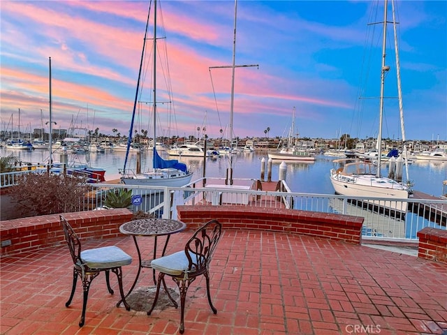 patio terrace at dusk featuring a water view and a dock