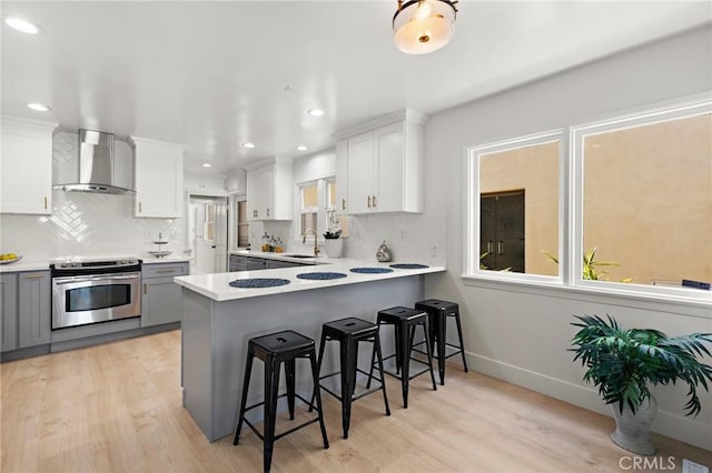 kitchen with stainless steel electric range, wall chimney exhaust hood, gray cabinetry, and white cabinets