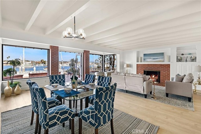 dining area with hardwood / wood-style flooring, a water view, beam ceiling, a notable chandelier, and a brick fireplace