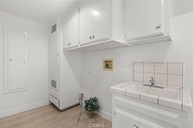 clothes washing area featuring sink, light wood-type flooring, washer hookup, and cabinets