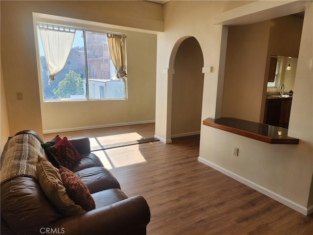 living area featuring arched walkways, baseboards, and wood finished floors