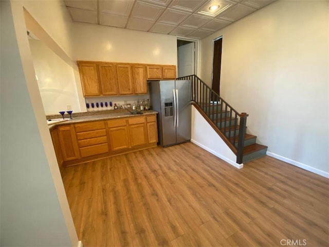 kitchen featuring stainless steel fridge, brown cabinetry, baseboards, and wood finished floors