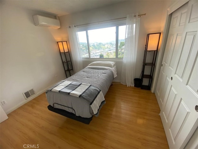 bedroom with visible vents, a wall mounted air conditioner, light wood-style flooring, and baseboards