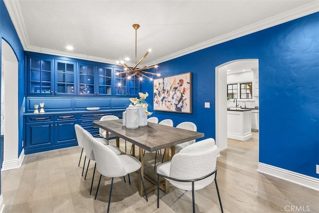 dining room featuring light wood finished floors, arched walkways, baseboards, crown molding, and a notable chandelier