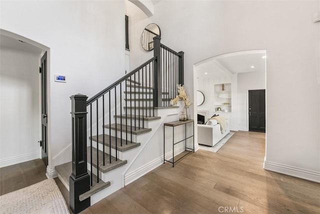 stairs featuring arched walkways, built in shelves, wood finished floors, and baseboards