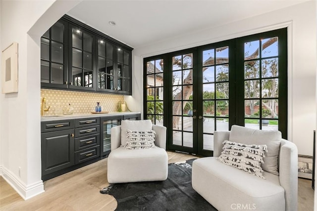 interior space with light wood-style flooring, a sink, baseboards, backsplash, and indoor wet bar