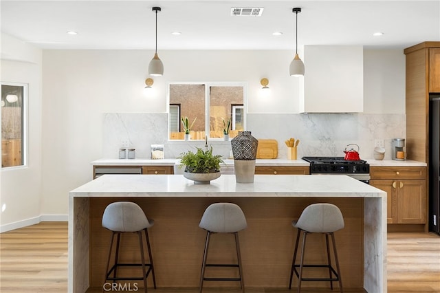 kitchen featuring a breakfast bar, visible vents, light wood-style floors, wall chimney exhaust hood, and range with gas cooktop