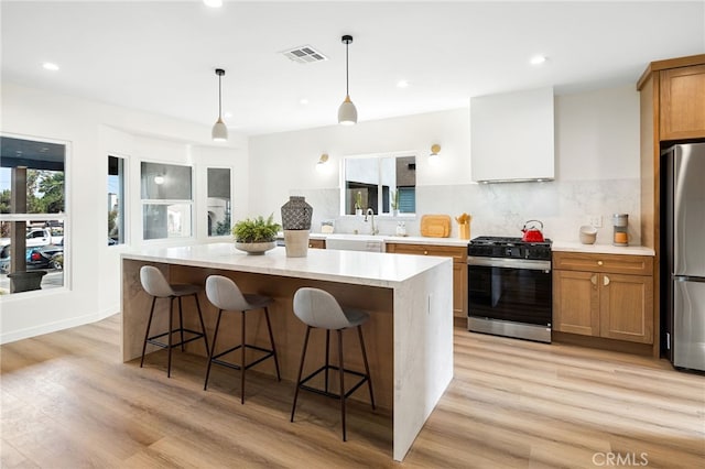 kitchen with range with gas stovetop, a center island, tasteful backsplash, visible vents, and freestanding refrigerator