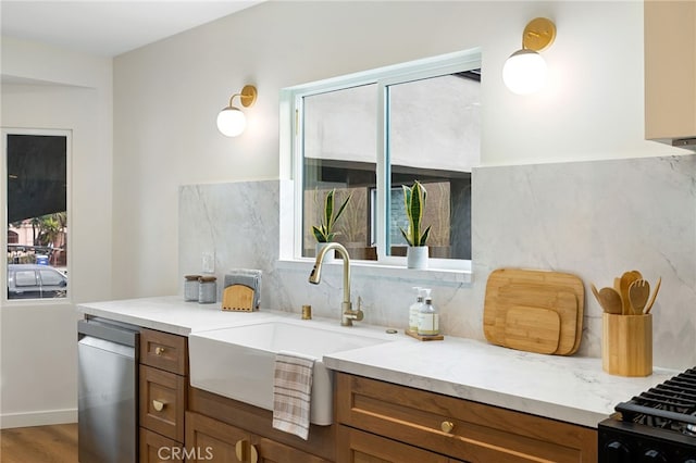 kitchen featuring tasteful backsplash, brown cabinetry, dishwasher, light stone countertops, and a sink