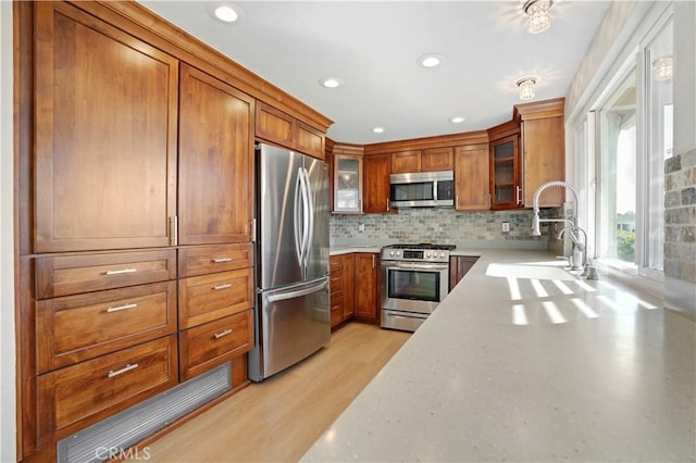 kitchen with brown cabinetry, glass insert cabinets, stainless steel appliances, light countertops, and a sink