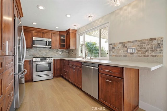 kitchen with light countertops, appliances with stainless steel finishes, brown cabinetry, glass insert cabinets, and a sink