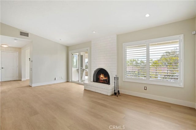 unfurnished living room featuring light wood finished floors, a brick fireplace, visible vents, and baseboards