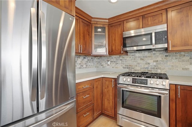 kitchen with decorative backsplash, glass insert cabinets, brown cabinets, appliances with stainless steel finishes, and light countertops