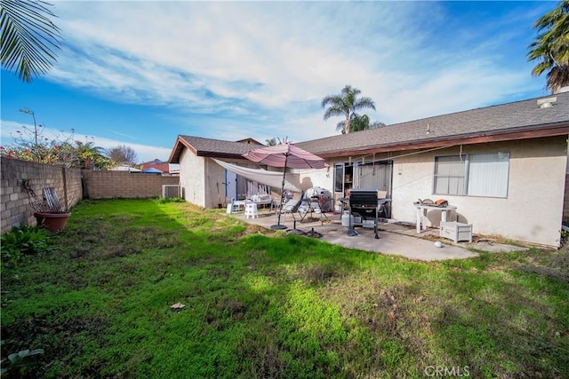 rear view of house with a fenced backyard, a yard, a patio, and stucco siding