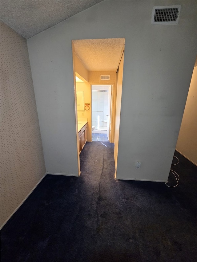 hall featuring visible vents, dark colored carpet, and a textured ceiling