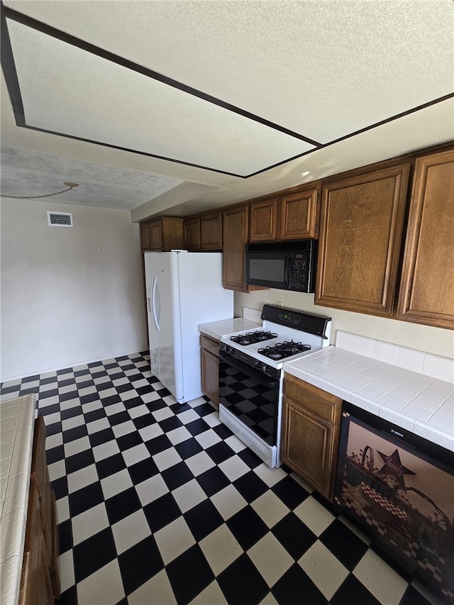 kitchen with visible vents, white appliances, a textured ceiling, tile counters, and light floors