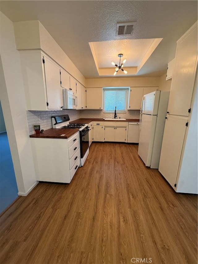 749 Junipero Ct, Merced, CA 95348 - kitchen with wood finished floors, a sink, a chandelier, a tray ceiling, and white appliances